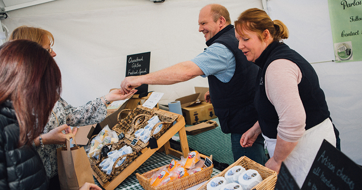 couple talking to customers at a market stall selling cheese